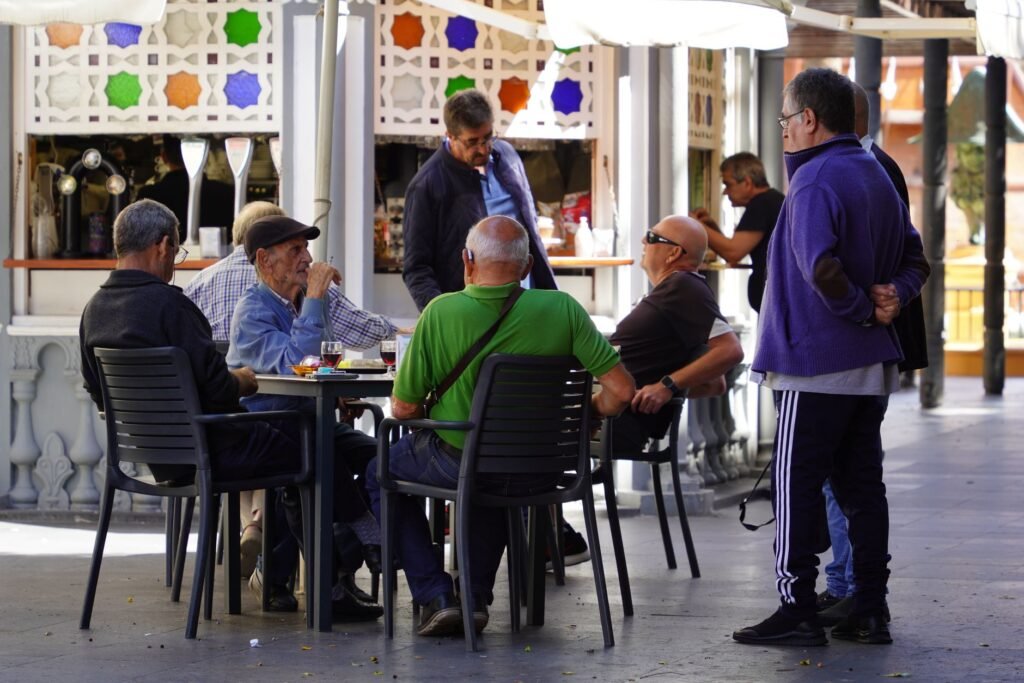 Twee volwassenen in gesprek aan een tafeltje op een plein in een Belgische stad