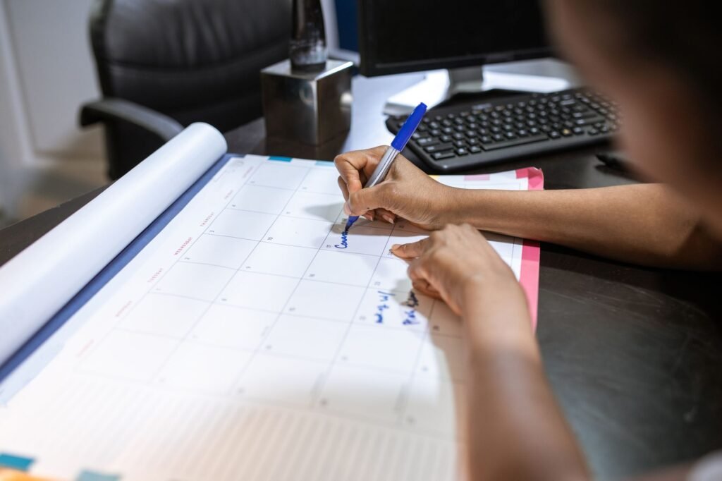 Personne prenant des notes à un bureau près d'une fenêtre, téléphone et calendrier visibles