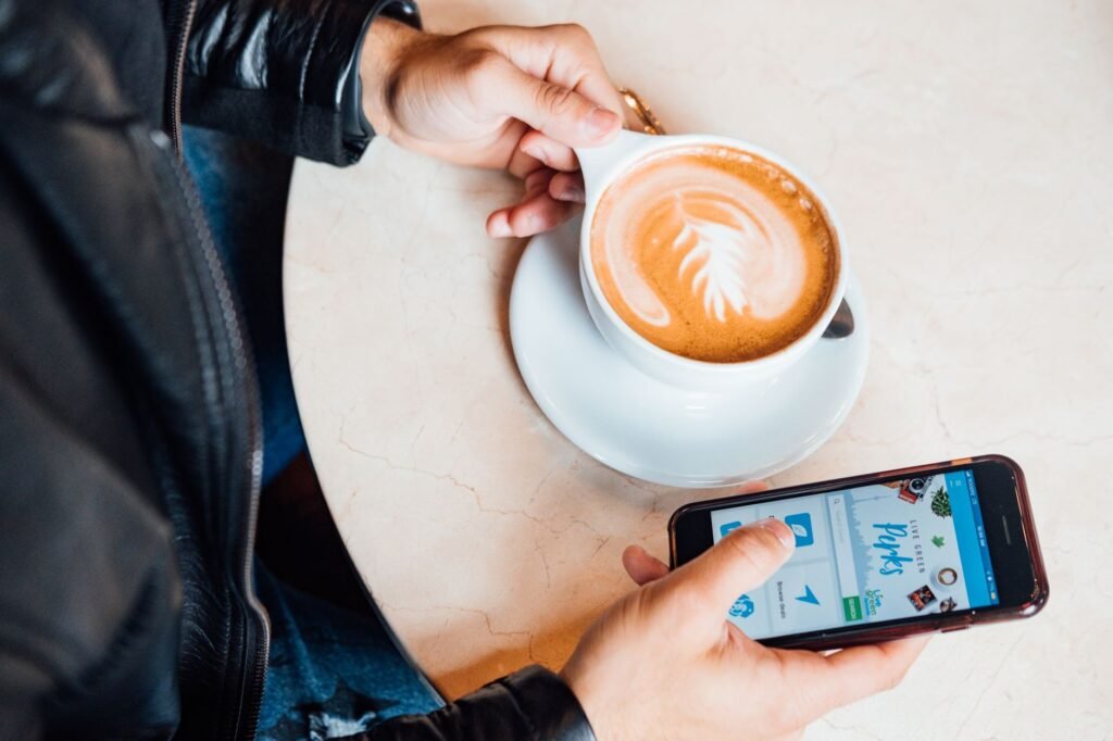 Smartphone op een houten cafetafel naast een kop koffie bij daglicht