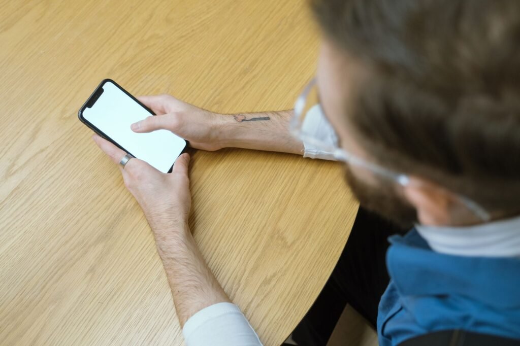 Handen die op een smartphone een bericht lezen aan een houten tafel bij daglicht