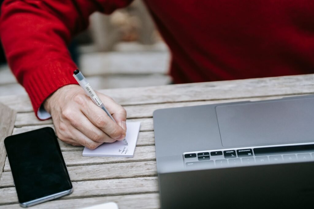 Persoon maakt notities aan een tafel met een smartphone, in een rustige huiselijke setting