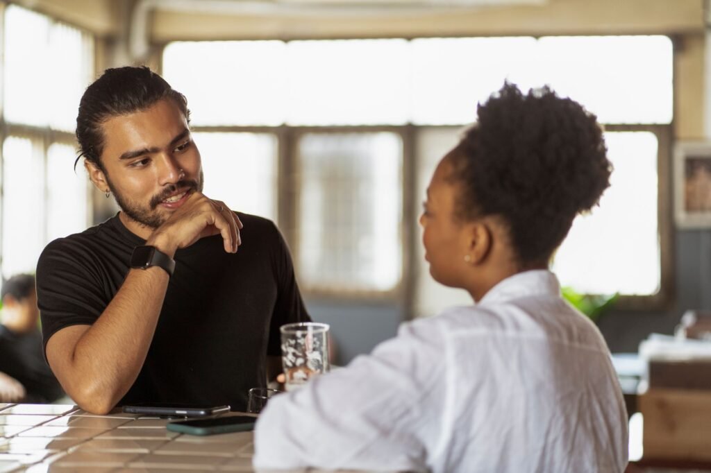 Twee volwassenen in gesprek aan een tafeltje in een warm verlicht cafΓ©