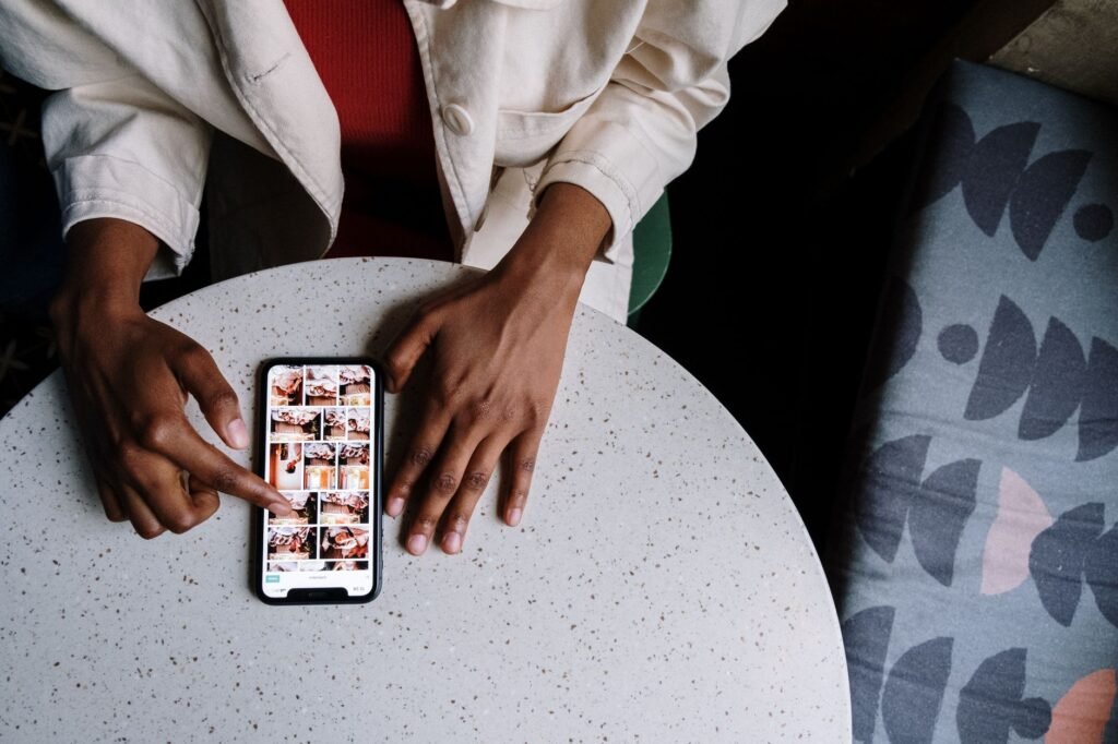 Personne consultant un annuaire sur son téléphone à une table de café, avec un carnet à côté