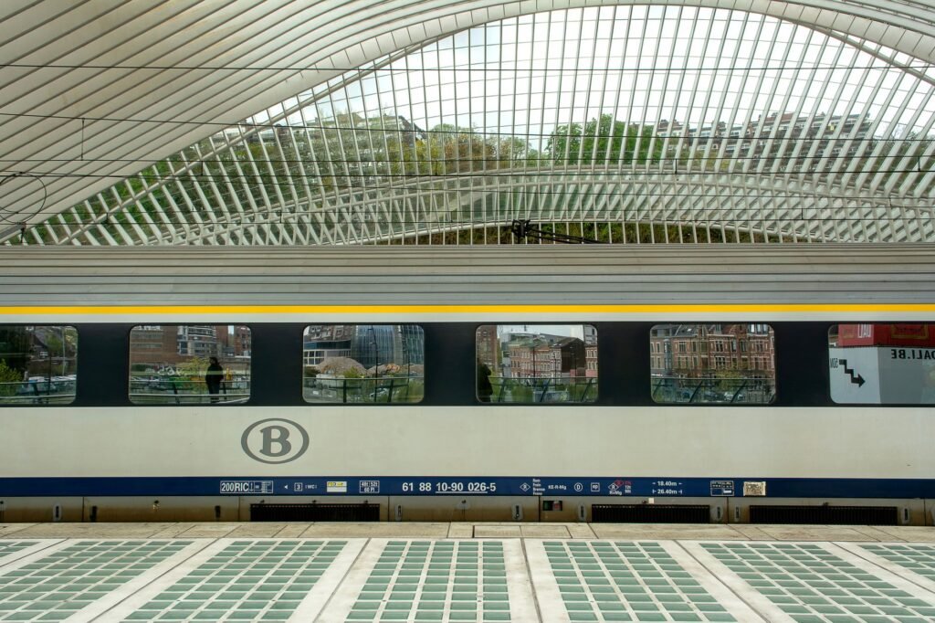 Perron van een Belgisch station overdag, met lege banken en vertrekbord
